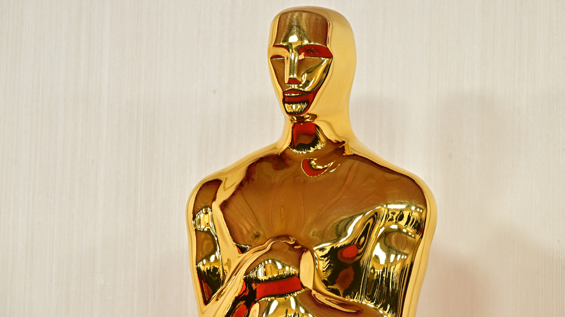 A close-up of a golden Oscar statuette against a light background.